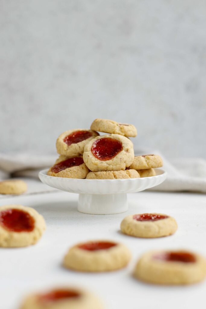 Almond Thumbprint Cookies on a white cakestand, red jam