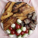 Grilled pineapple, tomato mozzarella and bacon-wrapped prunes sitting on a plate