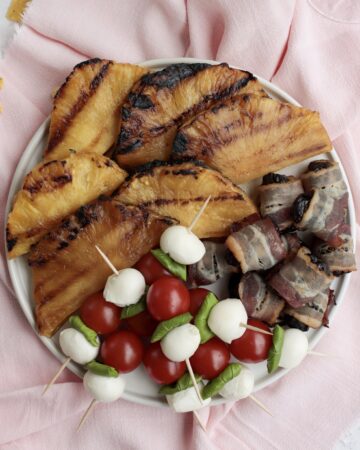 Grilled pineapple, tomato mozzarella and bacon-wrapped prunes sitting on a plate
