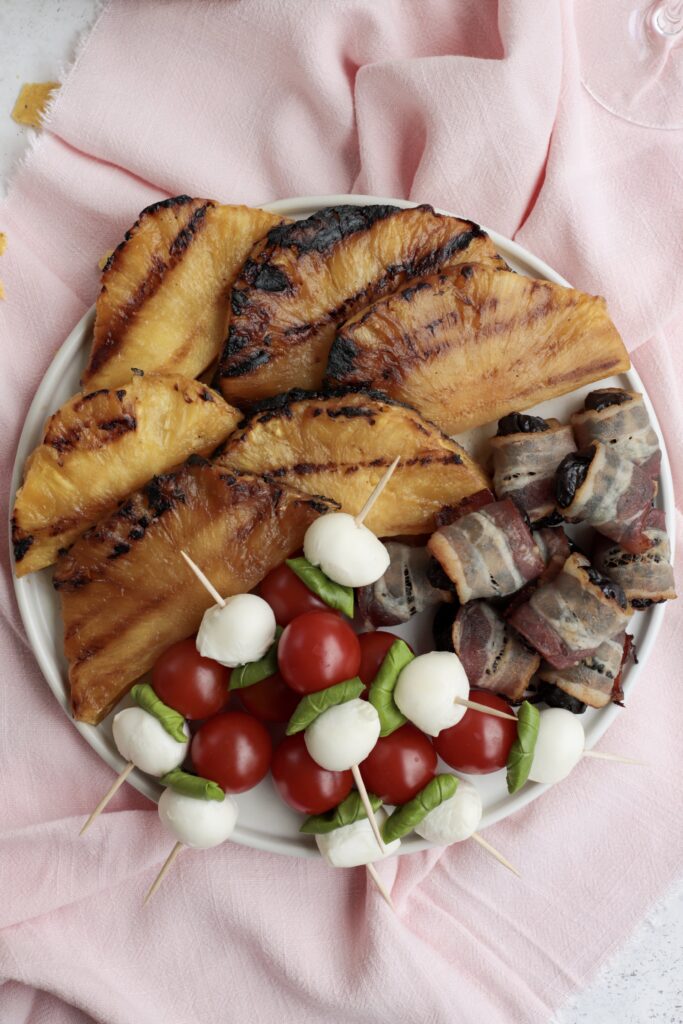 Grilled pineapple, tomato mozzarella and bacon-wrapped prunes sitting on a plate